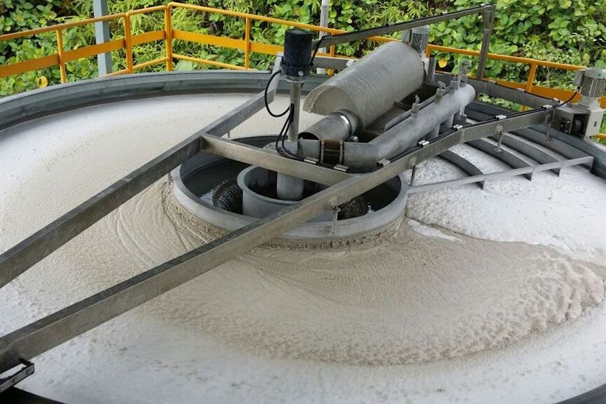 Industrial machinery mixing white material in a circular tank with railings in the background