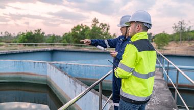 Two workers in hard hats inspect a water treatment tank, one pointing across the basin.