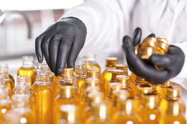 Black-gloved hands filling amber glass bottles in a bright production setting