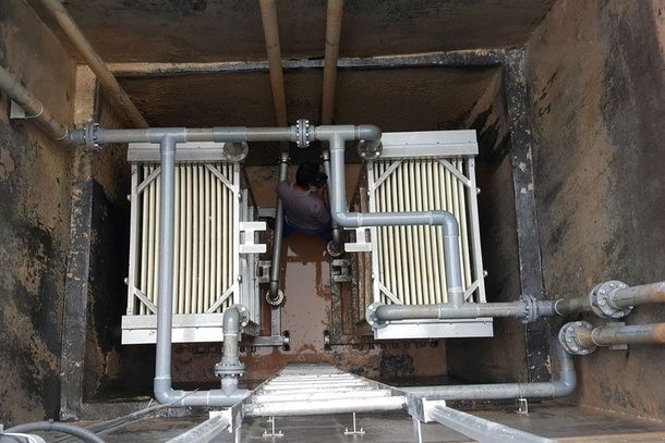 Overhead view of a worker crouched in a concrete pit beside gray pipes and stacked panels.