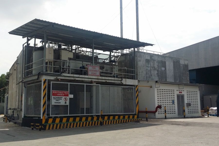 Industrial facility with metal roof, black-and-yellow barriers, and a small white building by the entrance