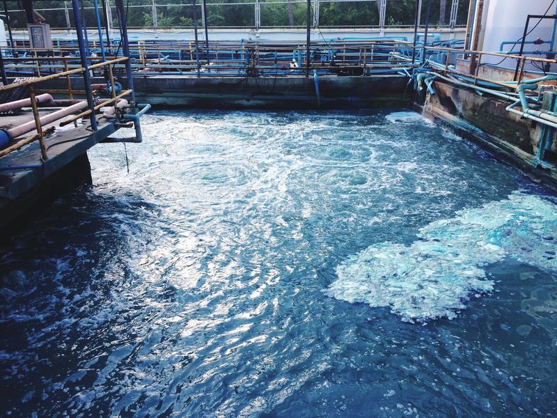 Large blue water tank with rippling water, surrounded by metal railings in an industrial setting