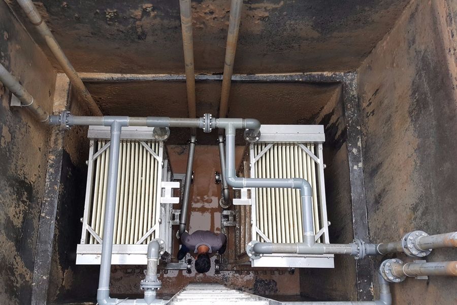 Rusty industrial pit with pipes, valves, and two cream-colored hose reels on a concrete floor
