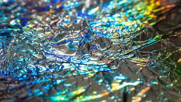Close-up of crinkled iridescent foil reflecting blue, gold, and silver light