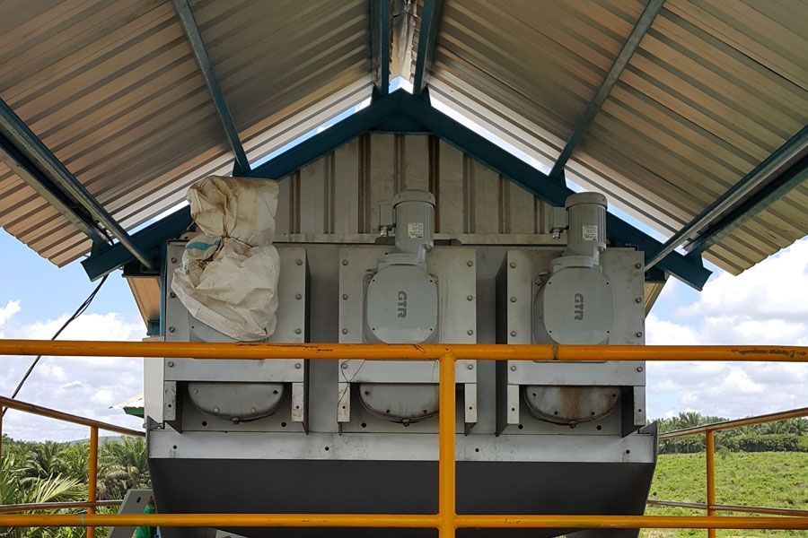 Industrial equipment under a corrugated metal shelter, with three gray units behind a yellow safety rail.