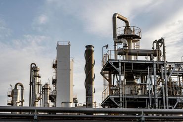 Industrial refinery with tall smokestacks, pipes, and metal structures under a cloudy sky