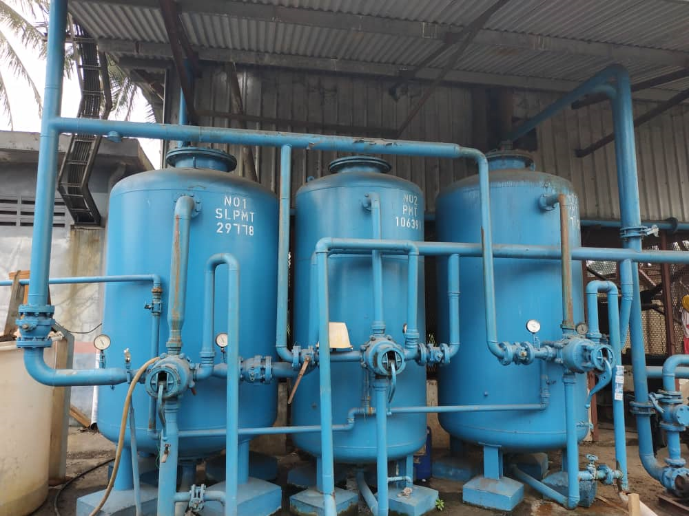 Blue industrial water treatment tanks with pipes and valves inside a factory shed