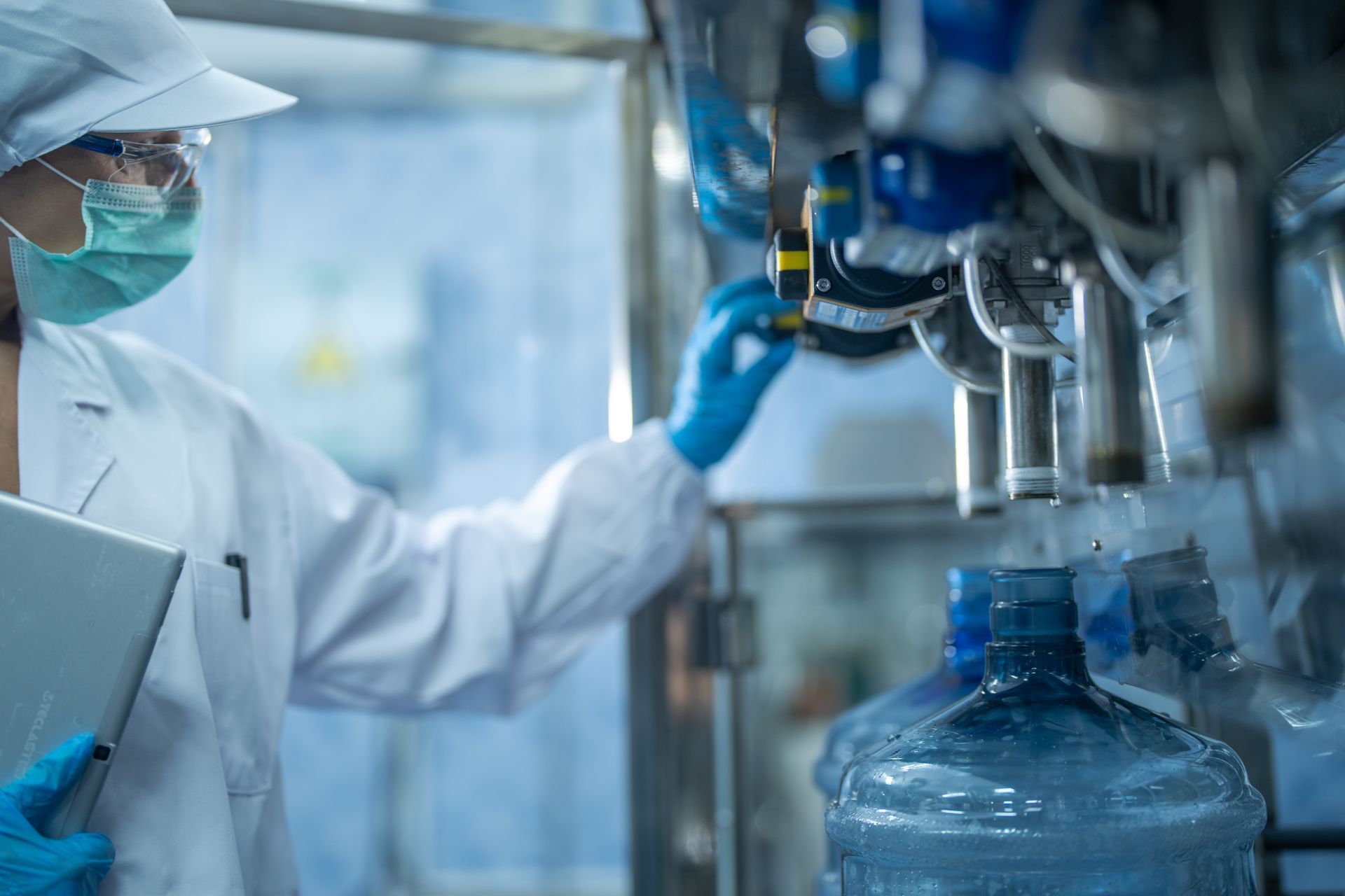 Lab technician in protective gear inspecting blue bottles on an industrial production line