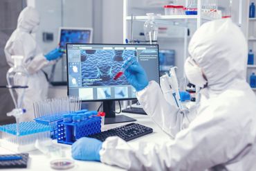 Scientists in a lab analyzing data on a monitor, with test tubes and equipment nearby.