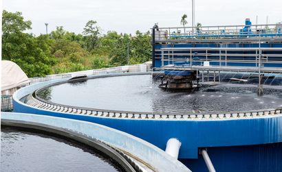 Large circular blue water treatment basin with dark water and metal scaffolding, surrounded by greenery
