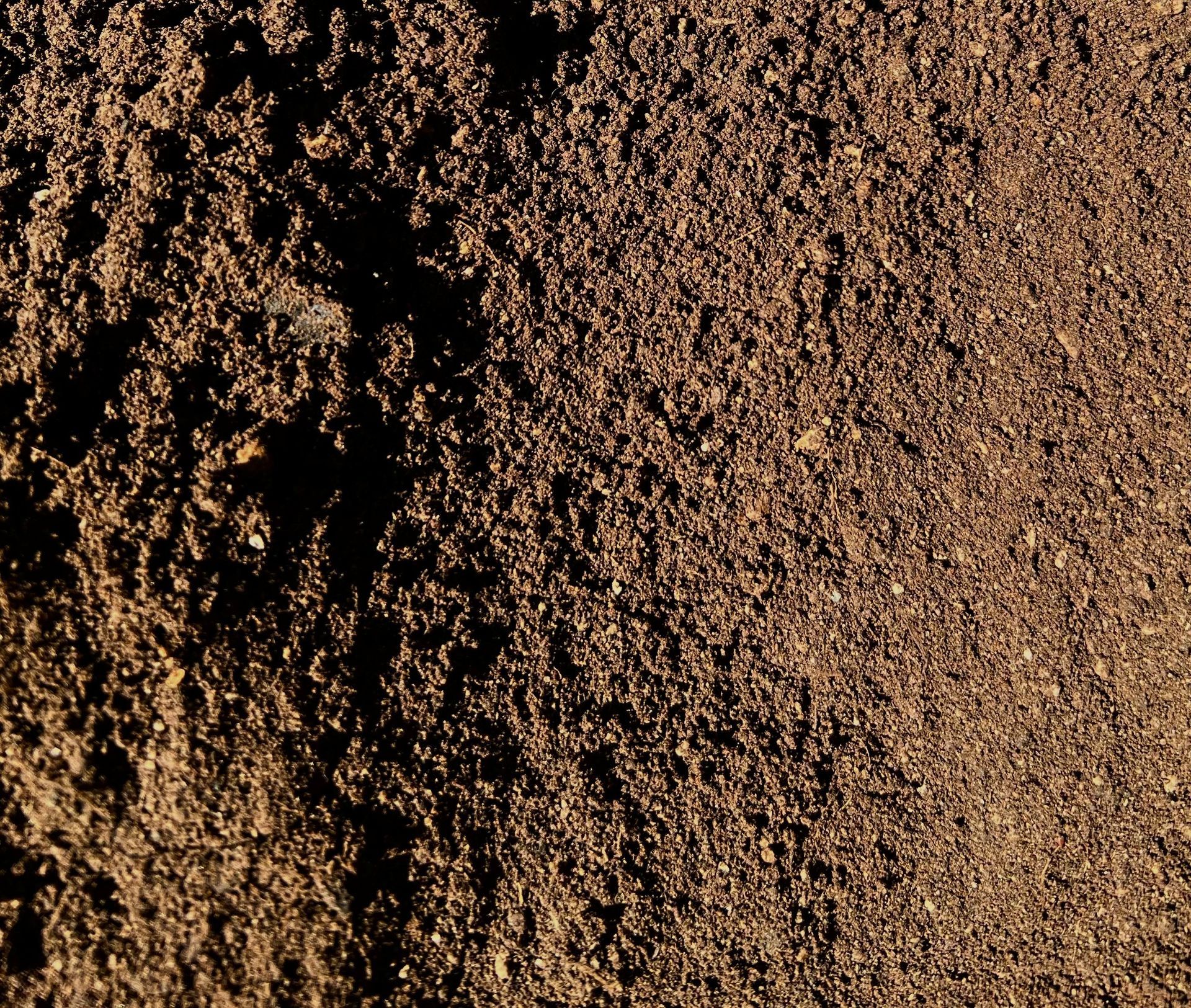 Close-up of dark, textured soil, showing a mix of small particles and a slightly coarse appearance.