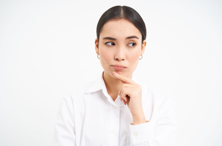 A woman in a white shirt is thinking with her hand on her chin.