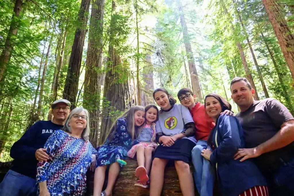 A group of people are sitting on a log in the woods.
