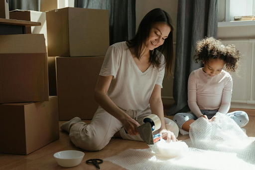 A woman and a child are sitting on the floor packing boxes.
