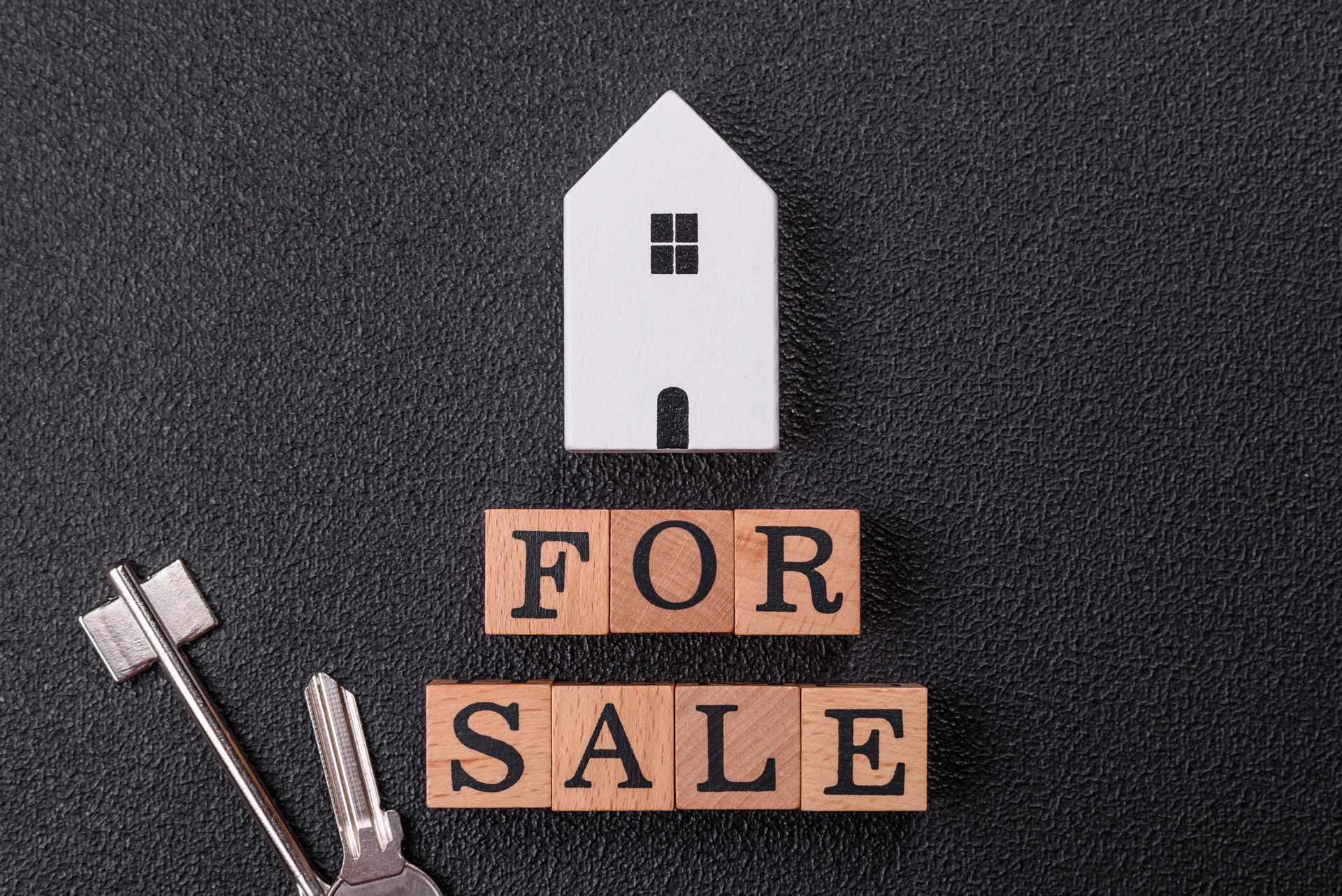 The word for sale is written on wooden blocks next to a house and keys.