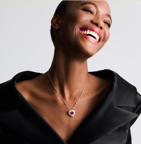 Modella sorridente con un top nero scollato sulle spalle e una collana con ciondolo a forma di cuore