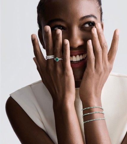 Persona sorridente con le mani sul viso, che indossa gioielli d’argento e un top bianco senza maniche.