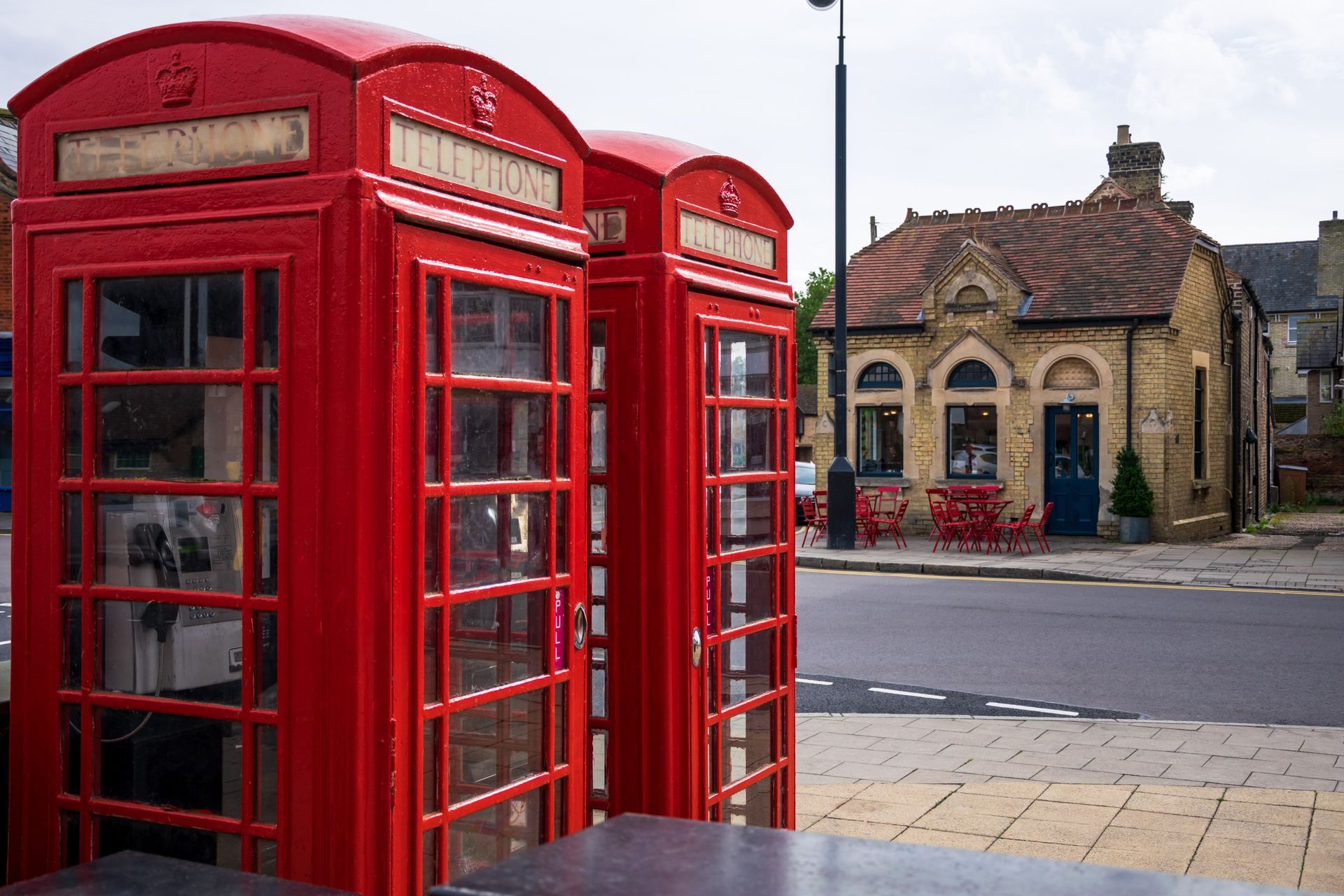 Red British phone booths on a sidewalk, with a tan building in the background.