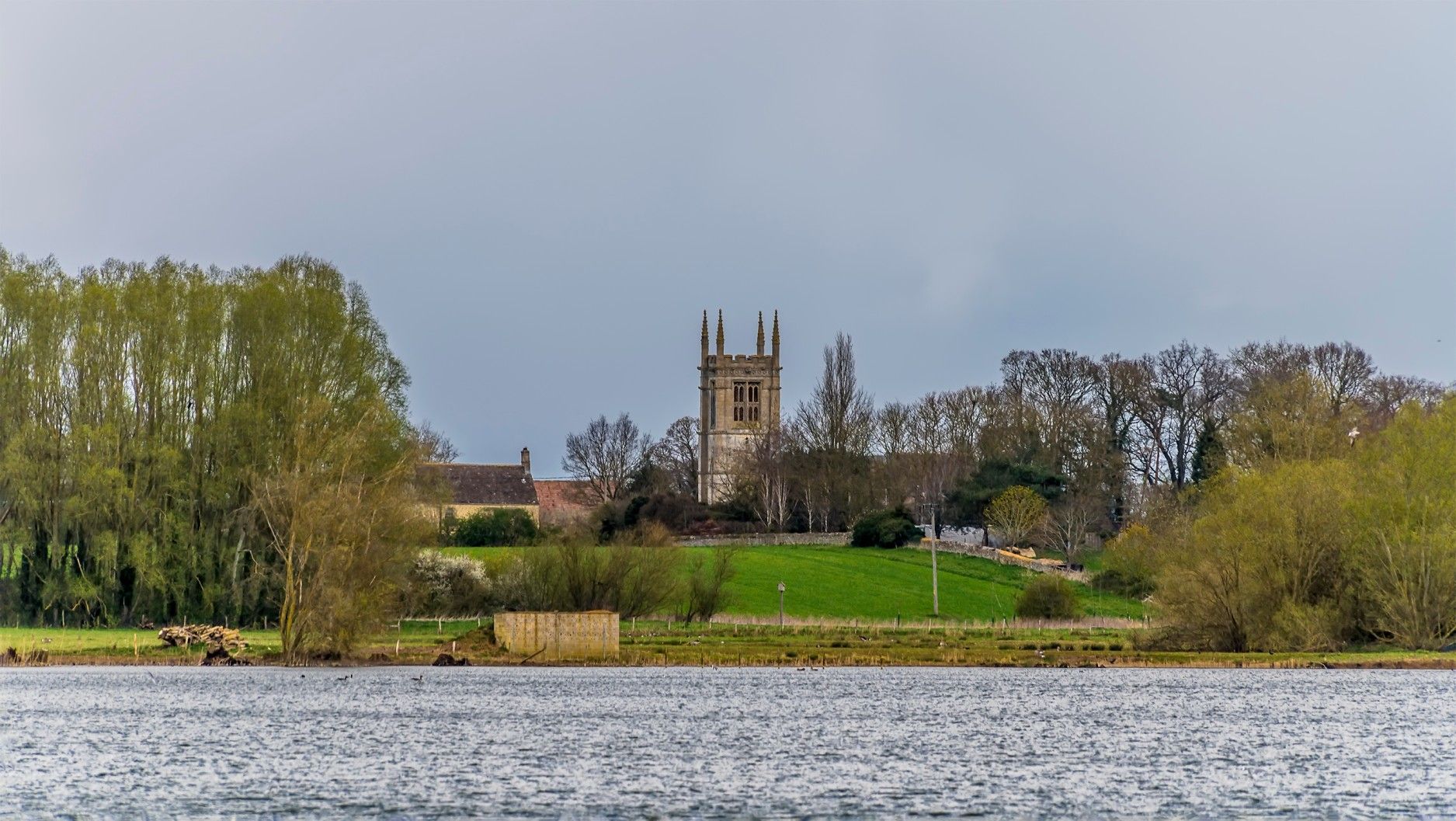 Church tower on a hill, viewed from across a body of water under an overcast sky.