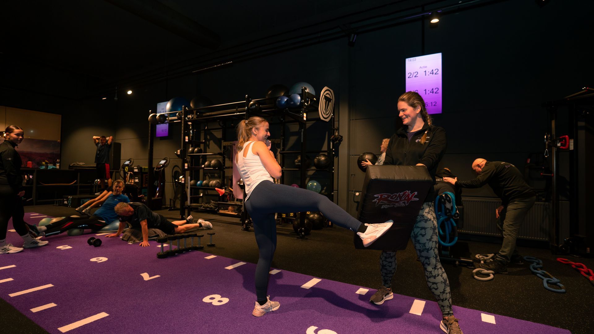 Mensen die sporten in een sportschool met paarse vloer, gewichten en fitnessapparatuur.