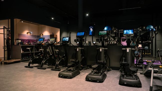 Een schemerig verlichte sportschool met rijen loopbanden, hometrainers en gewichtsapparaten.