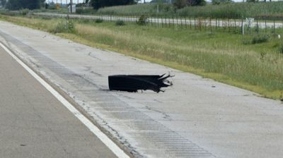 Collapsed black roadside drainage grate on a highway shoulder beside grass.