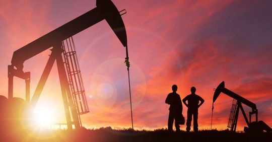 Silhouetted oil pumpjacks and workers at sunset against a red-orange sky