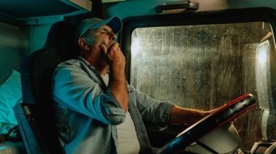 Driver talking into a radio inside a truck cab, looking out a rain-speckled window