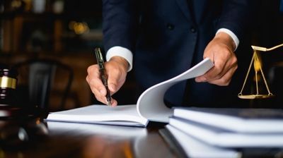 Lawyer signing documents at a desk with a scales of justice in the background