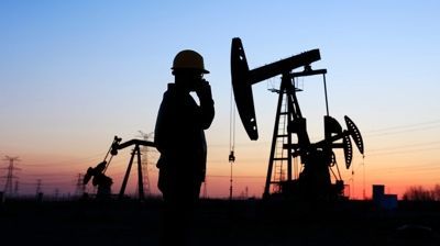 Silhouette of oil pumpjacks and a worker at sunset in an oil field