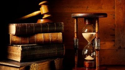 Stacked law books, a gavel, and an hourglass on a wooden table, lit warmly