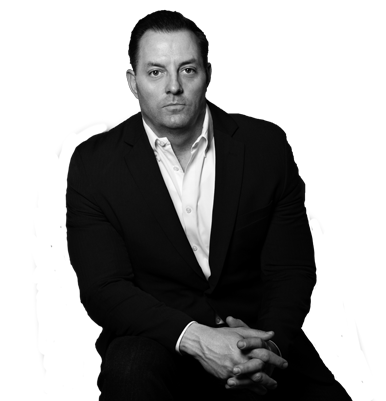 Black-and-white portrait of a man in a dark suit, seated with hands clasped against a plain background