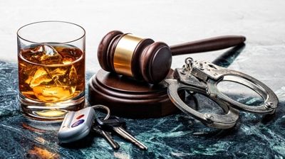 Whiskey glass, judge’s gavel, handcuffs, and car key fob on a marble surface
