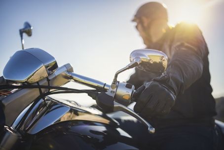 Motorcyclist riding a black bike at sunset, with bright sun glare on the chrome