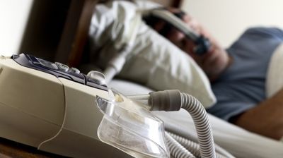 CPAP machine hose in foreground beside a person resting in bed