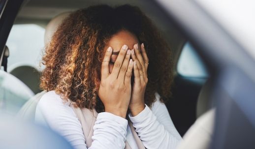 Person sitting in a car with face in hands, appearing stressed or upset.