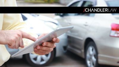 Person using a tablet near a car accident scene with an insurance logo in the corner