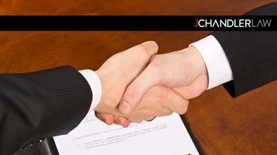 Two businesspeople shaking hands over a document on a desk, symbolizing an agreement
