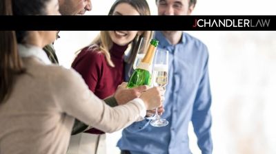 People clinking champagne glasses at a social event, with a J. Chandler Law banner above.