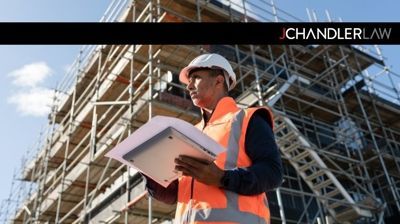 Construction worker in orange vest and hard hat reviewing plans at a building site.