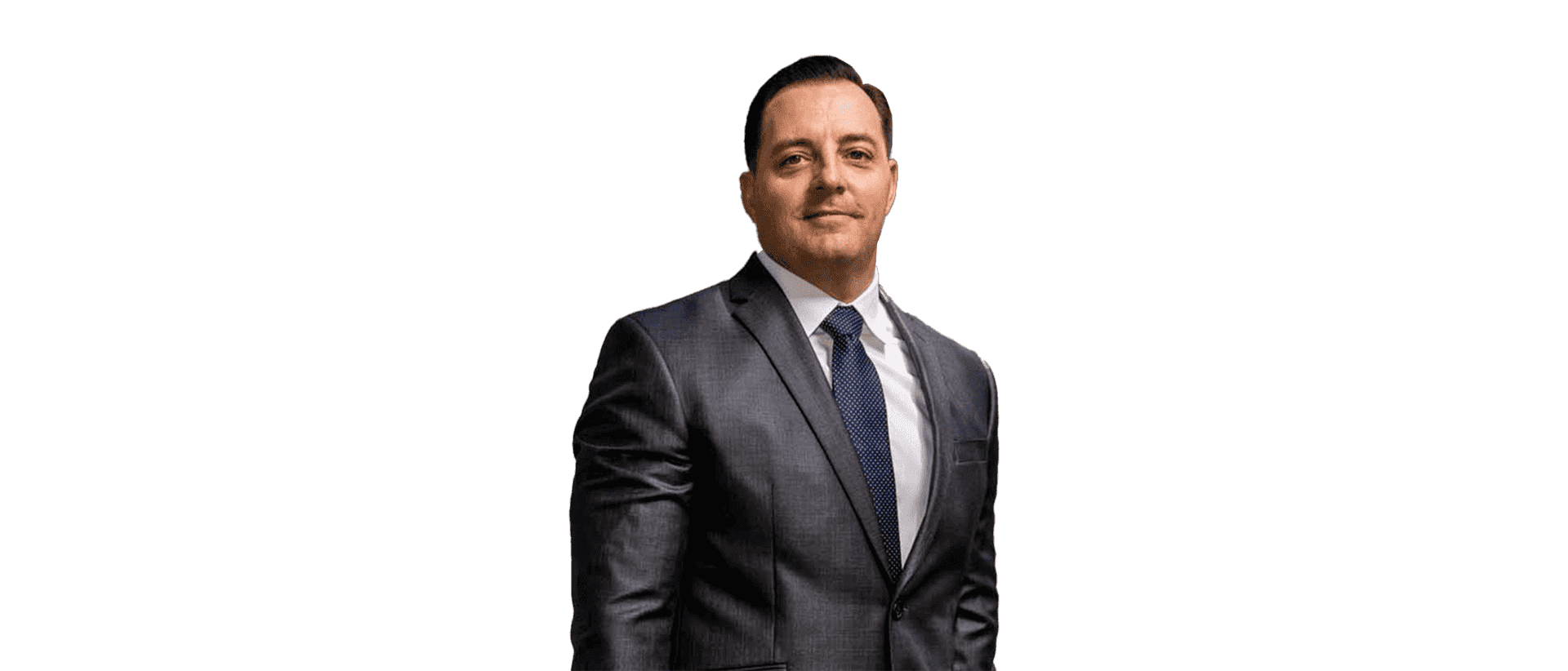 Man in a dark suit and tie standing against a white background, facing forward with a neutral expression