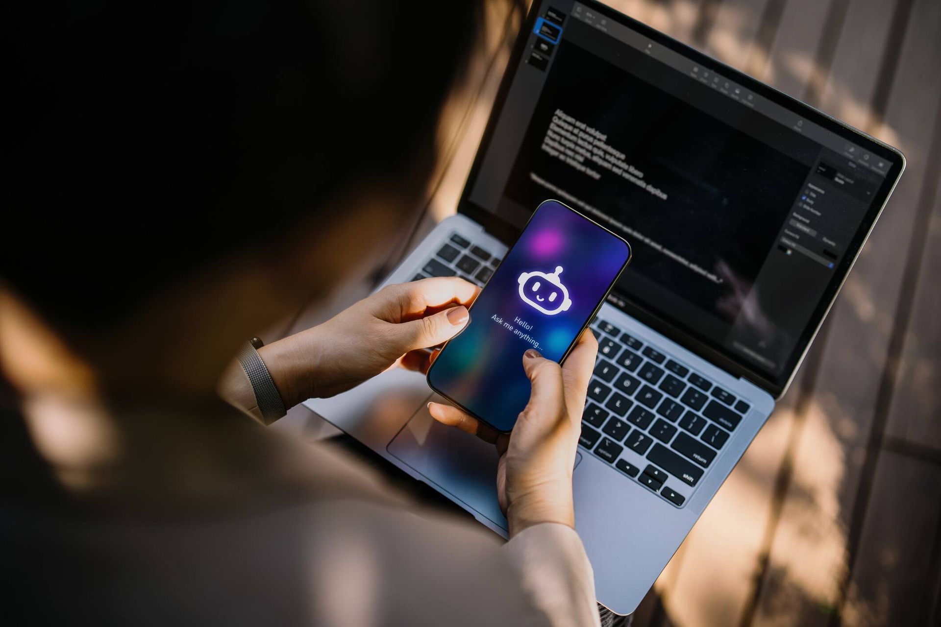 Persona que sostiene un teléfono con el ícono de la aplicación, usando una computadora portátil al aire libre.