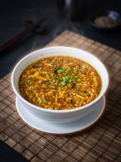 White bowl of spicy soup topped with herbs on a woven placemat