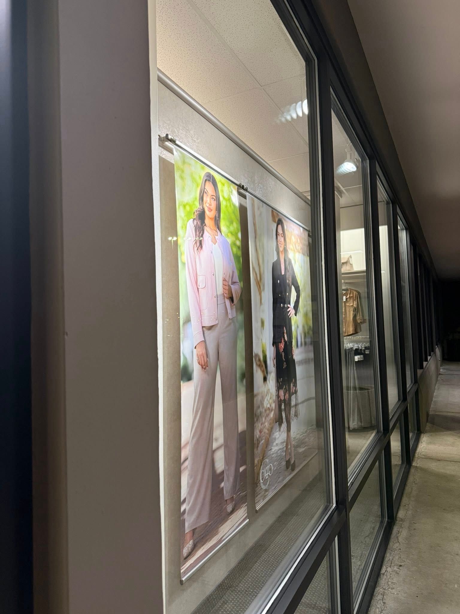 Wall of framed fashion posters in a lit indoor corridor with a tiled floor