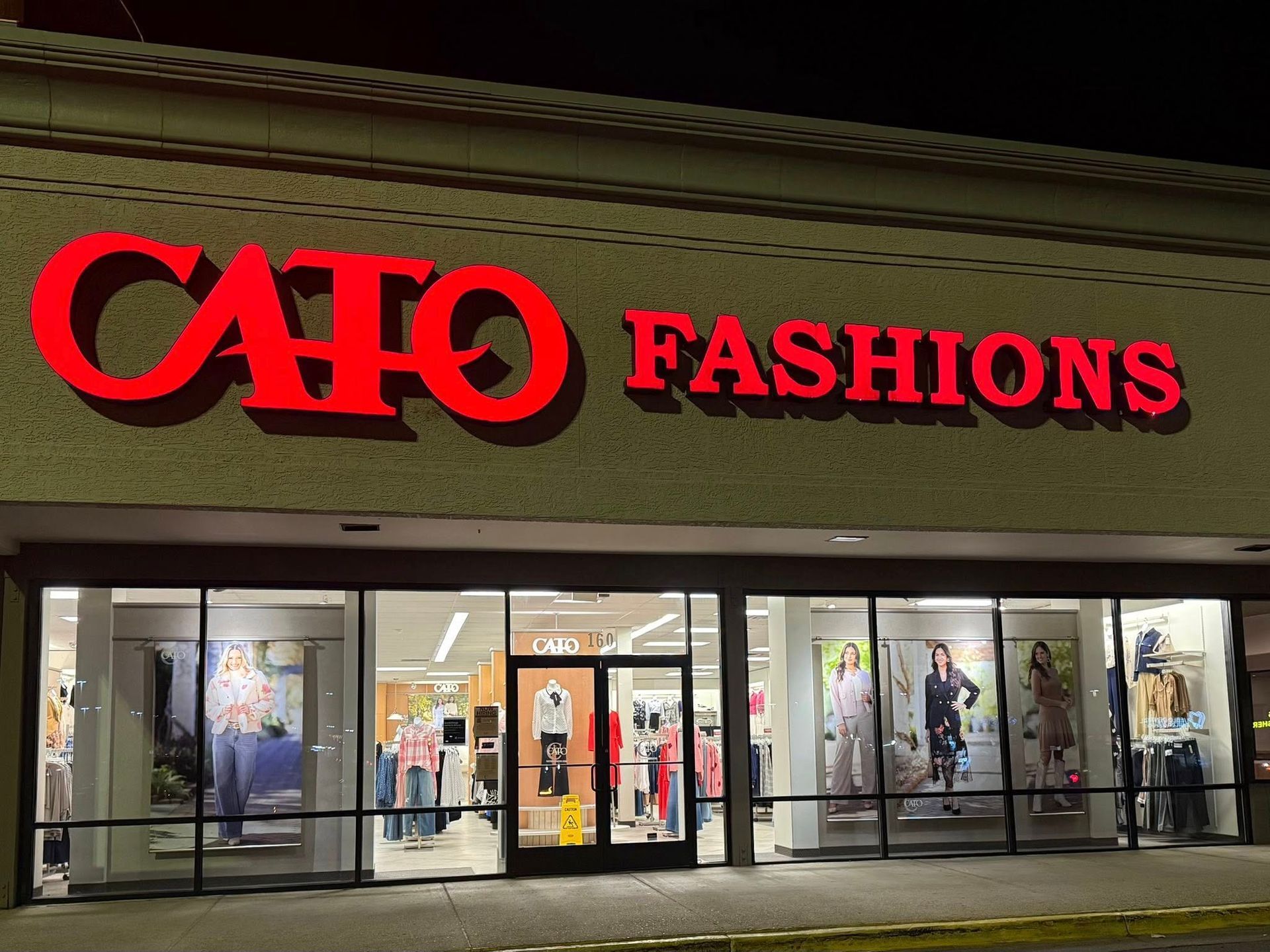Cato Fashions storefront at night with red illuminated sign and lit display windows