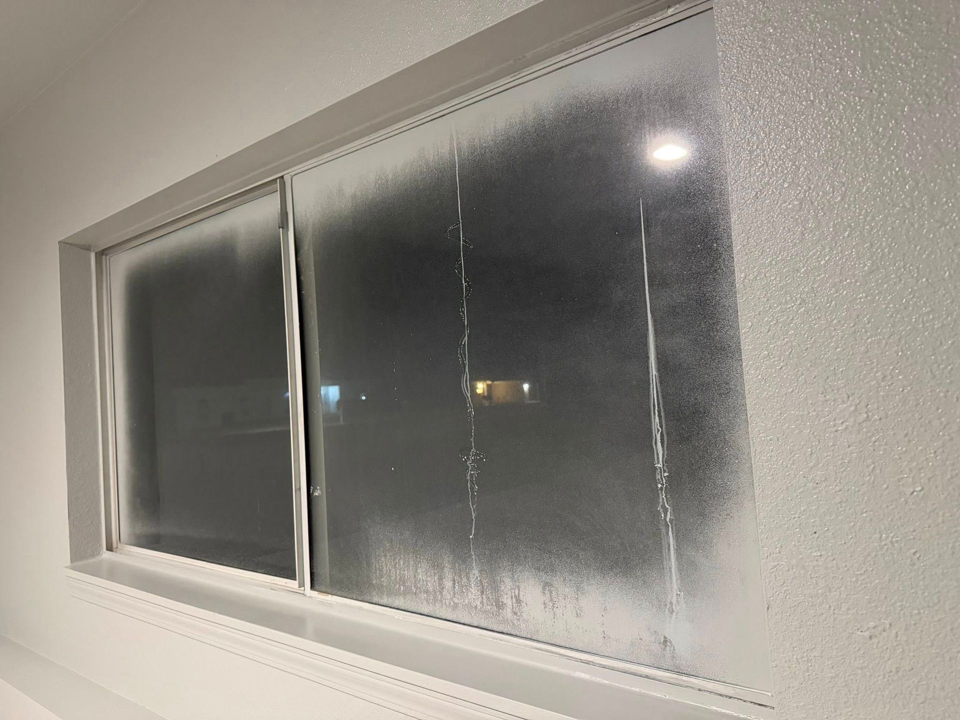 Frosted window with a few bright reflections and a white frame inside a dim room