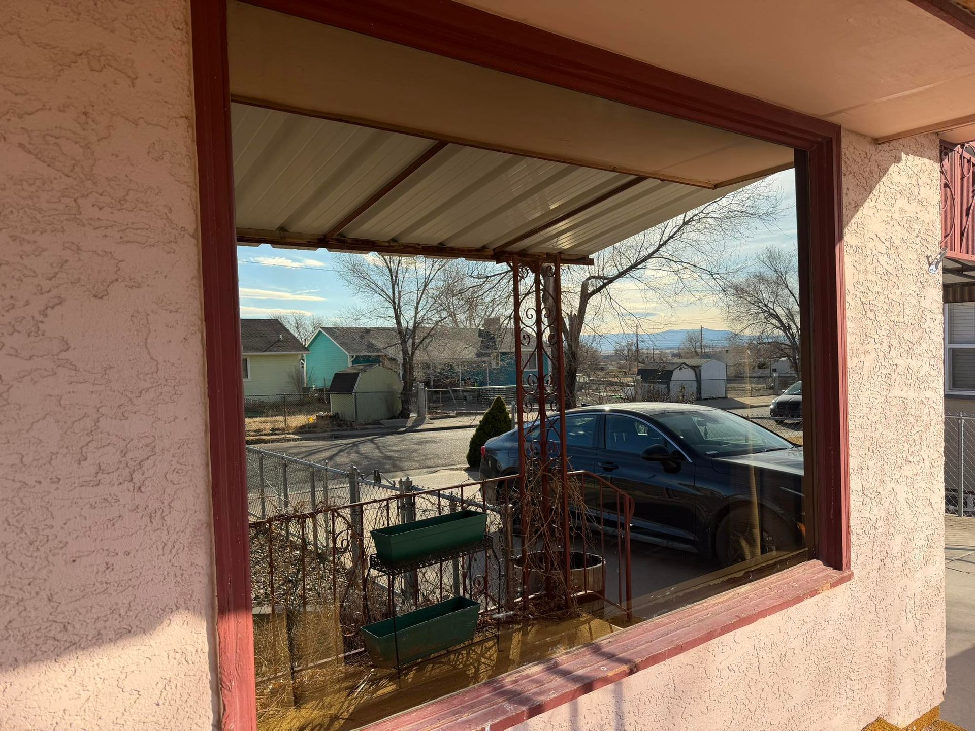 View through a window to a parked car, snowy street, and houses on a sunny day