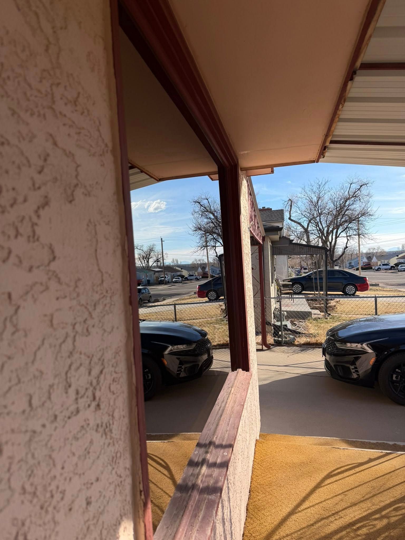 Covered porch overlooking parked cars and leafless trees on a sunny day.