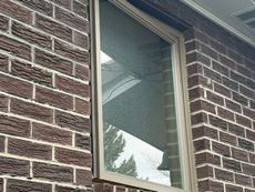 Partially open window in a brick wall with a screen and reflected trees