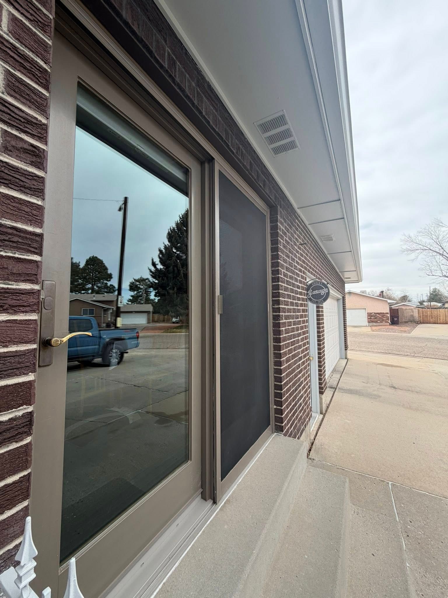 Storefront windows and brick facade along a sidewalk, with a blue truck reflected in the glass.